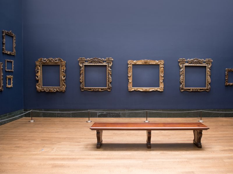 Sala de exposición con marcos dorados en la pared y una banca
